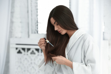 Beautiful young woman applying serum onto her healthy long hair at home