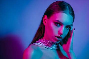 Naklejka na ściany i meble High fashion model in colorful bright neon lights posing at studio. Portrait of beautiful girl with trendy glowing make-up. Art design vivid style.