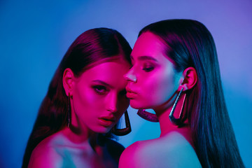 High fashion models in colorful bright neon lights posing at studio. Portrait of beautiful girls with trendy glowing make-up. Art design vivid style.