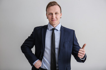 Handsome stylish businessman showing thumb-up on light background