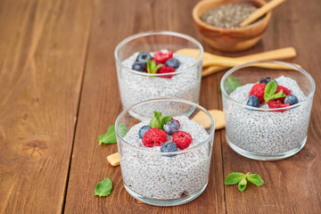 Chia pudding with fresh berries raspberries, blueberries. Side view, three glass on brown wooden background, copy space.