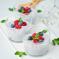 Chia pudding with fresh berries raspberries, blueberries. Three glass, light background, side view, flowers, close up.
