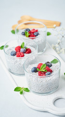 Chia pudding with fresh berries raspberries, blueberries. Three glass, vertical, light background, side view, flowers.