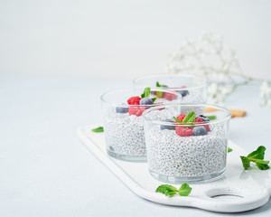 Chia pudding with copy space, fresh berries raspberries, blueberries. Three glass, light background, side view, flowers.