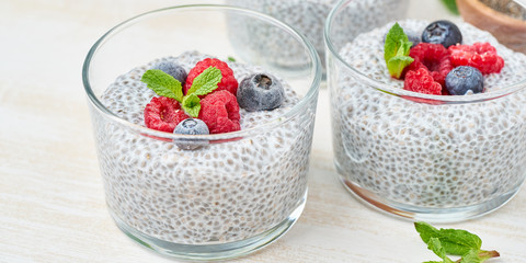 Banner with chia pudding with fresh berries raspberries, blueberries. Three glass, light wooden background, side view, flowers, close up.