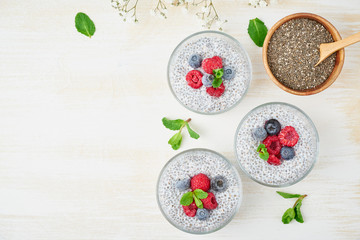 Obraz na płótnie Canvas Chia pudding, top view, copy space, fresh berries raspberries, blueberries. Three glass, light wooden background, flowers, close up.