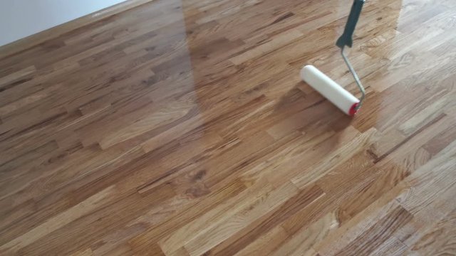Varnishing lacquering parquet floor by paint roller - second layer. Home renovation parquet. Varnish paint roller strokes on a wooden parquet. Application of a highly glossy parquet lacquer