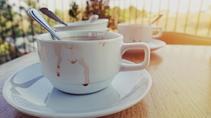 Empty dirty cup of coffee, glasses, a plates remained after eating and drinking drinks on a wooden table in the rays of the bright sun, in a street cafe.
