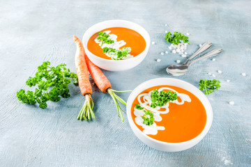 Spring vegetable soup. Homemade carrot cream soup, with fresh organic carrots, sour cream and herbs, blue concrete background copy space