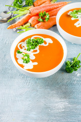 Spring vegetable soup. Homemade carrot cream soup, with fresh organic carrots, sour cream and herbs, blue concrete background copy space