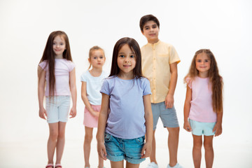 Fototapeta premium The portrait of happy cute little kids boy and girls in stylish casual clothes looking at camera against white studio wall. Kids fashion and human emotions concept