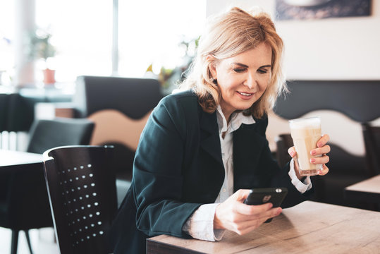 Attraktive &auml;ltere Frau sitzt im Cafe und checkt ihr Handy 