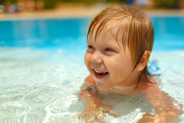 Fototapeta na wymiar Smiling blond-haired toddler lying in the swimming pool