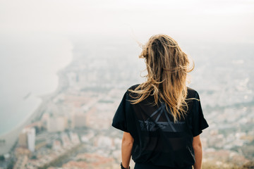 Young woman on top of the mountain looking at the city from above