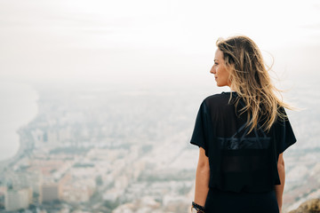 Young beautiful woman on top of the mountain looking at the city from above