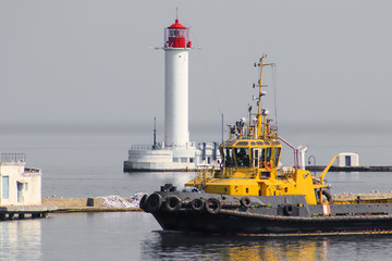 Marine tugboat  coming out of harbor seaport on lighthouse background. Cargo port of Odessa, Ukraine