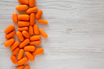 Peeled baby carrots ready to eat on a white wooden background, top view. Overhead, from above, flat lay. Copy space.