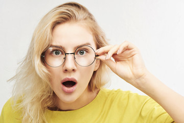 Surprised woman in round glasses with open mouth and bulging eyes looks into camera and sees...