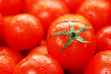 Ripe red tomatoes, with drops of dew. Close-up background with texture of red hearts with green tails. Fresh cherry tomatoes with green leaves.