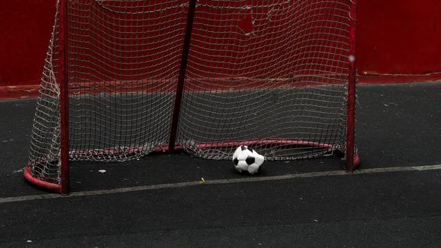 Broken half deflated soccer ball fly to small goal gate with weary net, slow motion shot. No goal keeper, ball roll into and check the goal.