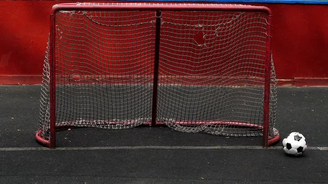 Broken soccer ball roll out of empty goal gate, bad shot, slow motion. Ball slowly roll and stop on white line beside steel bar