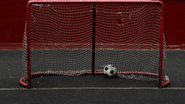 Broken soccer ball fly into five-a-side goal gate, catch mesh and fall down, nobody defending gate. Slow motion shot of poor game episode