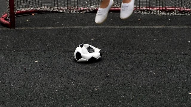 Angered woman crush and jump on deflated soccer ball, then kick it away, slow motion shot of white boots on black field, standing against small goal gate. Failed game or bad luck concept