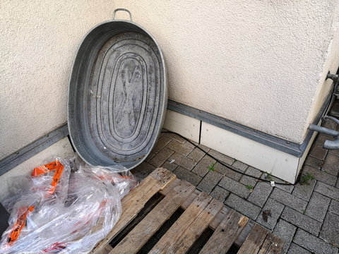 Alter grauer Waschzuber aus Blech, angelehnt an eine Hauswand in Naturfarben und alte Europalette aus Holz in einem Hinterhof im Westend von Frankfurt am Main in Hessen