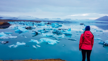 A young woman standing on the side of the glacier lagoon. Huge and massive ice bergs are slowly...