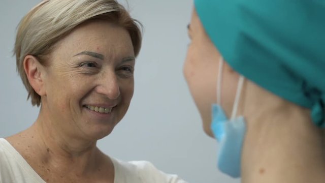 Smiling elderly lady hugging nurse, remission after fatal disease, good news