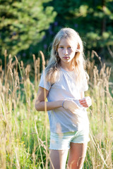 teen blonde white girl standing on green summer outdoor meadow