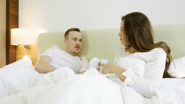 Young happy man and woman drinking coffee, talking, smiling and laughing in the bed. 4K