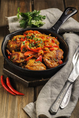 Fried chicken in spicy sauce with vegetables. Cooked in a cast iron pan. The pan is on a dark wooden background. Next is a natural linen napkin. Vertical.