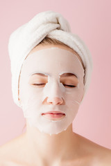 Beautiful young woman is applying a cosmetic tissue mask on a face on a pink background. Healthcare and beauty treatment and technology concept