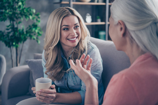 Close up photo two people she her ladies rumours mom granddaughter child granny hot beverage tea hands conversation tell speak say funky life stories sit comfy couch divan flat house indoors