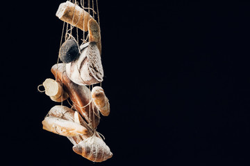 Obraz na płótnie Canvas fresh baked bread, baguettes and croissant with flour hanging on ropes isolated on black with copy space