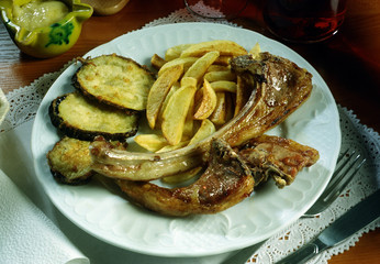 Plato con costillas de cordero, berenjenas y patatas fritas.