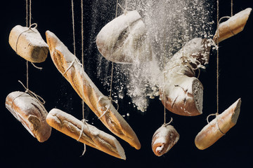 white flour falling at fresh baked bread hanging on ropes on black background