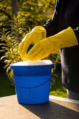 Spring Cleaning outside with big yellow cleaning gloves, water, soap and a big blue bucket with soap. Cleaning the table. Soap Foam on the table. Hands in bucket. Holding and wringing cleaning sponge. © Pepijn
