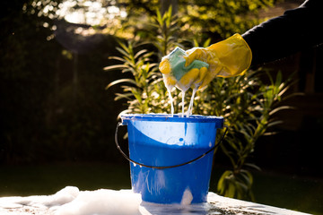 Spring Cleaning outside with big yellow cleaning gloves, water, soap and a big blue bucket with...