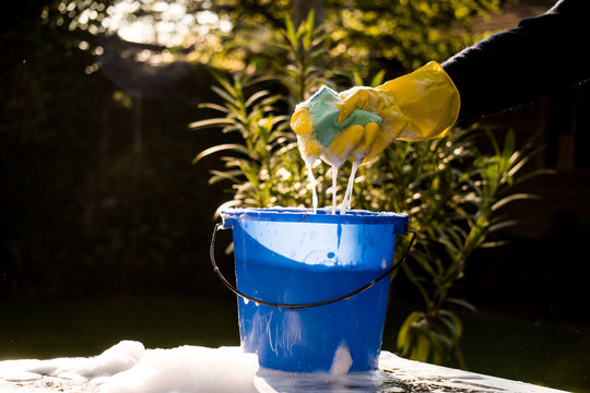 Spring Cleaning Outside With Big Yellow Cleaning Gloves, Water, Soap And A Big Blue Bucket With Soap. Cleaning The Table. Soap Foam On The Table. Hands In Bucket. Holding And Wringing Cleaning Sponge.