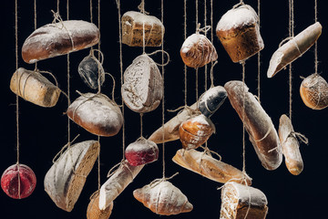 white and brown bread and pastry hanging on ropes isolated on black
