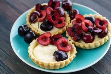 Cherry and custard tartlets on a blue plate. Dark wooden table, high resolution