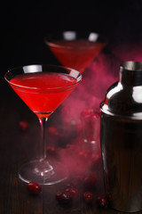 Cosmopolitan cocktail with cranberries, shaker and jigger on a dark wooden table. High resolution,...