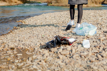 Young woman collecting plastic trash from the beach and putting it into black plastic bags for recycle. Cleaning and recycling concept.