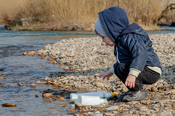 Save environment concept, a little boy collecting garbage and plastic bottles on the beach to dumped into the trash.