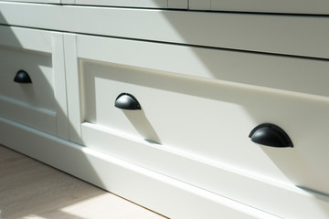 Black handle on the white door of the cabinet.