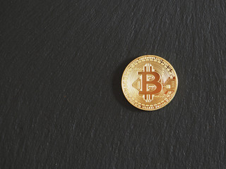 Close up of a gold bitcoin coin on a black textural background. copy space.