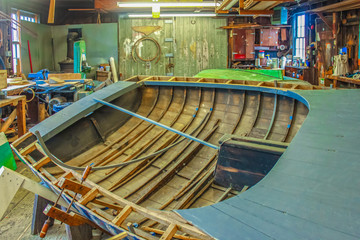 Partially built wooden boat in dark old marina workshop with fluorescent lights - selective focus and bright light glare in windows