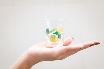 Young woman holding a small glass with multi-colored pills inside